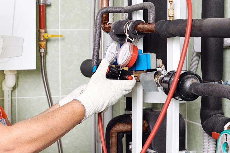 A person providing home maintenance inspection services by checking a heating system in a boiler room.