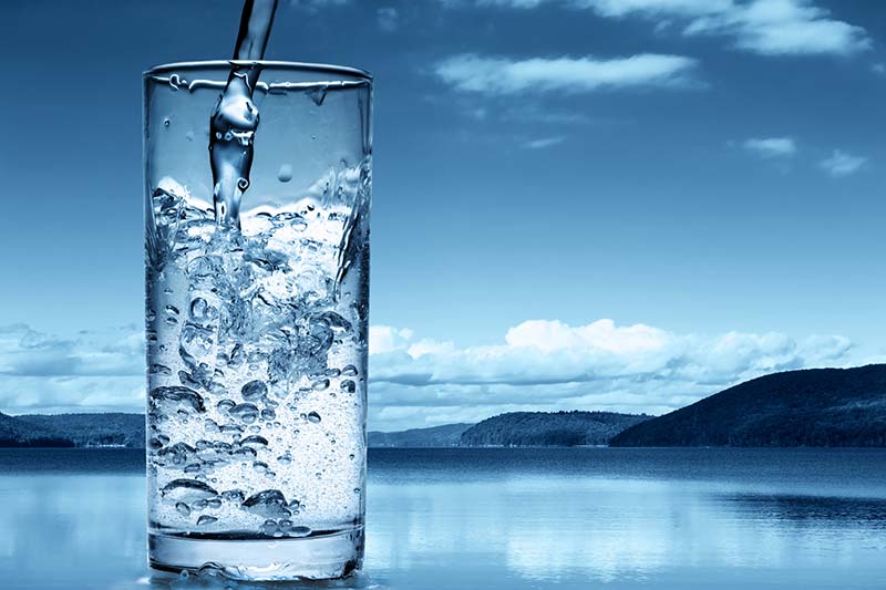 A water glass being filled with a lake and mountains scene in the background